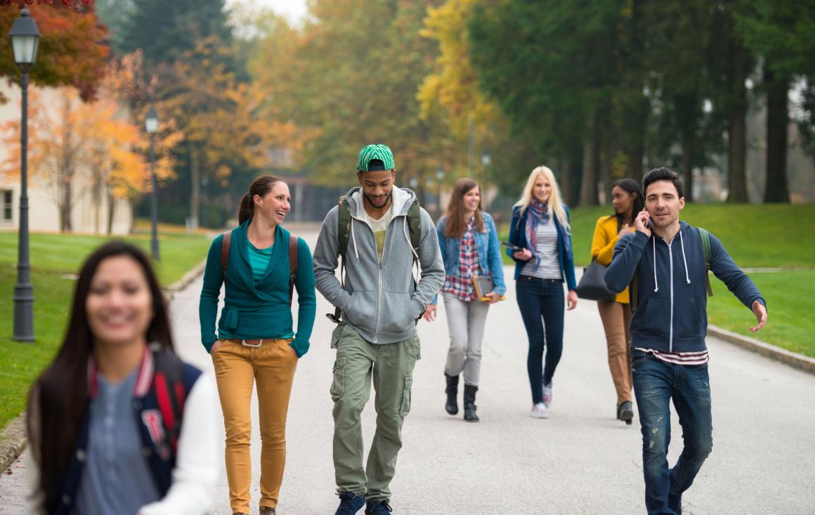 Students walking on a college campus, with one student talking on the phone, as part of the Evaluating the Healthier Campus Initiative