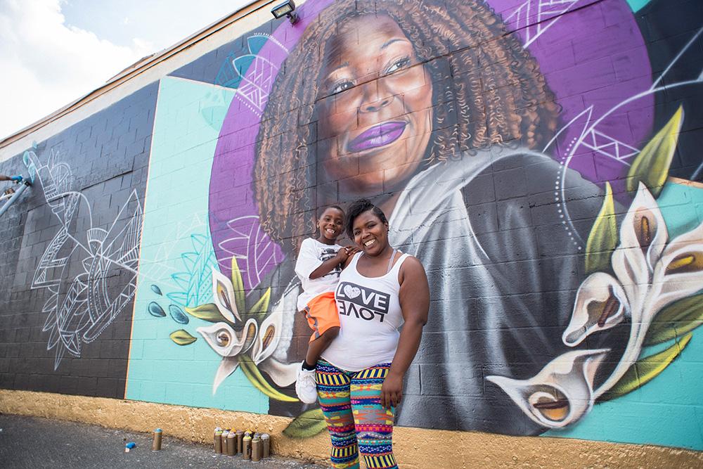 A mother holding her child while standing in front of a colorful mural