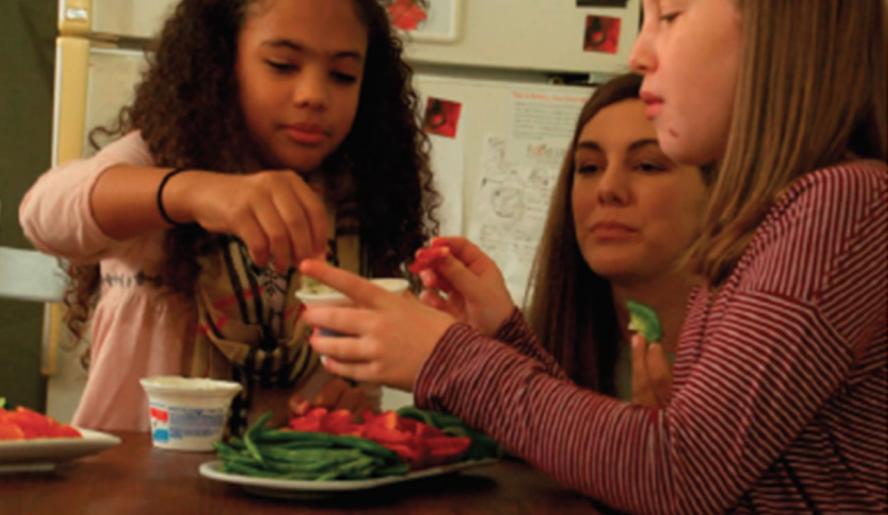 Professor Folta observing as one kid holds a dip container and another dips a vegetable, with more vegetables on a plate on the table