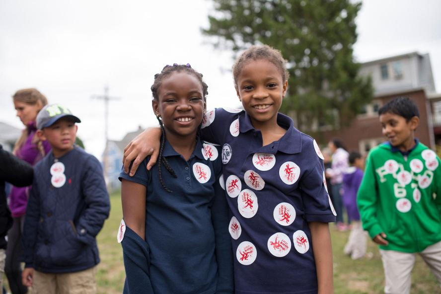 Two children standing and smiling, with others children and adults in the background