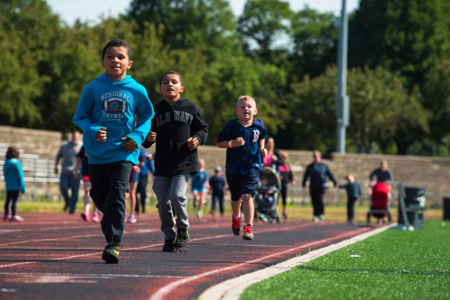 Kids running on a track with parents coming behind, some pushing strollers