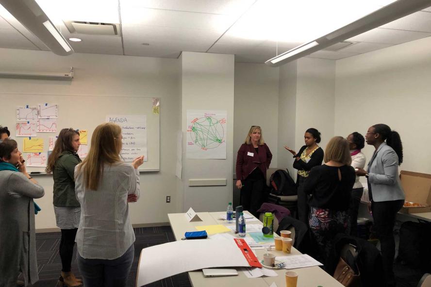 A group of people gathered in a room, discussing ideas with papers pinned on the wall behind them