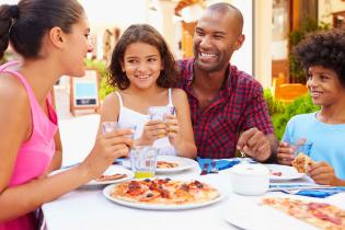 Children and their parents eating pizza in a restaurant, smiling and looking at each other