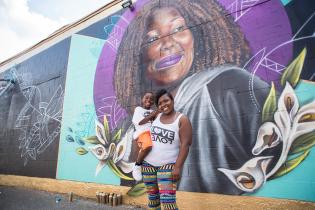 A mother holding her child while standing in front of a colorful mural