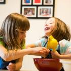 One child is squeezing a lemon with a juicer, while the other watches the lemon juice dripping into a bowl