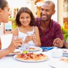 Children and their parents eating pizza in a restaurant, smiling and looking at each other