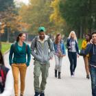Students walking on a college campus, with one student talking on the phone, as part of the  Evaluating the Healthier Campus Initiative